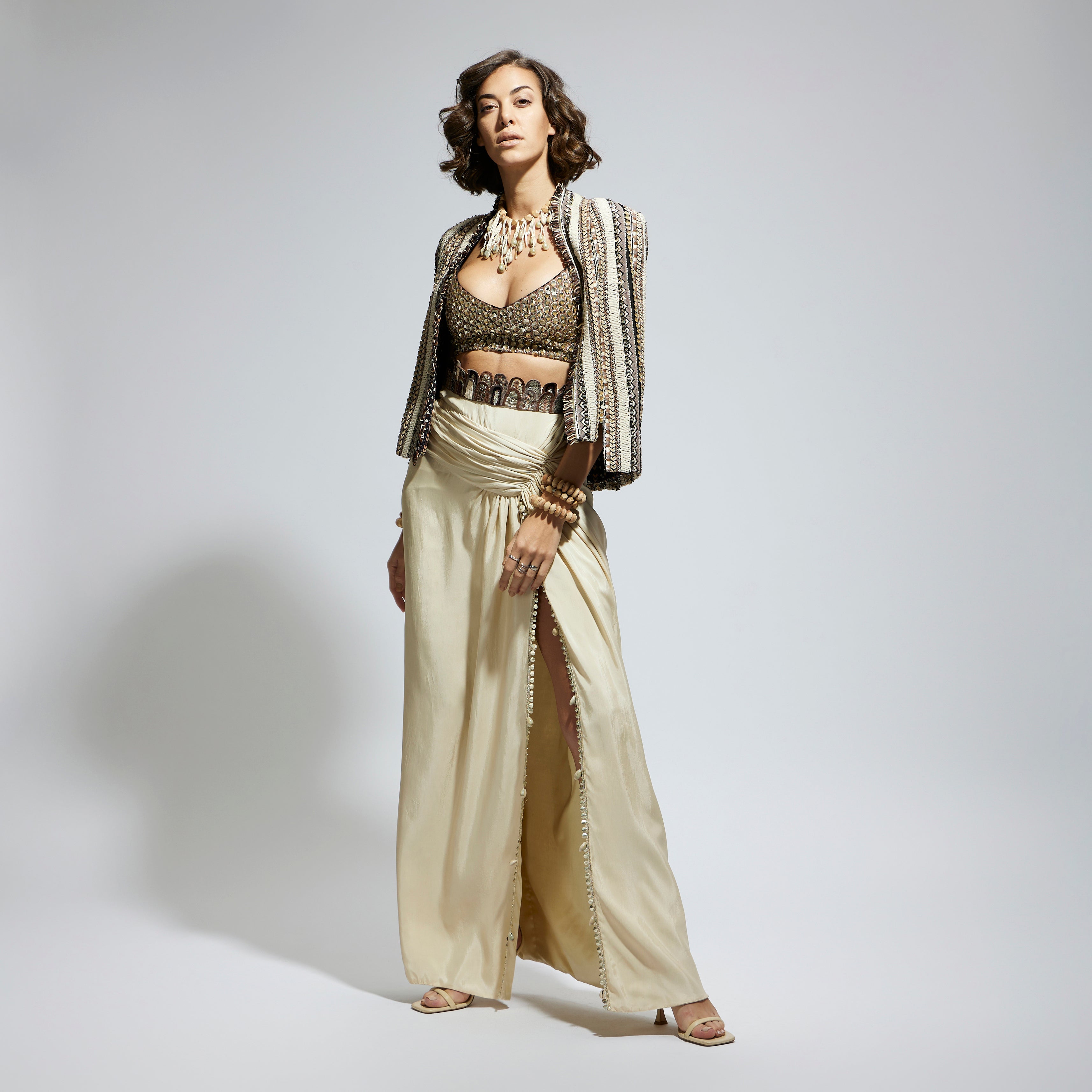 EMBELLISHED & TEXTURED CAPE JACKET PAIRED WITH METALLIC SCALLOP BUSTIER AND IVORY HIGH SLIT SKIRT